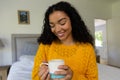 Happy biracial woman in yellow sweater holding cup of coffee at home Royalty Free Stock Photo