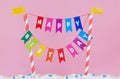 Happy Birthday banner on candy striped poles standing in white icing covered with sprinkles