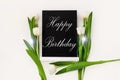 Happy Birthday card message sign on black chalkboard with tulip flowers on white background flat lay. Blackboard text Royalty Free Stock Photo