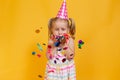 Happy birthday child girl in pink cup blowing confetti on colored yellow background. Celebration, childhood Royalty Free Stock Photo