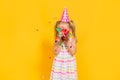 Happy birthday child girl in pink cup blowing confetti on colored yellow background. Celebration, childhood. Royalty Free Stock Photo