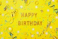 Happy birthday greeting text decorated with confetti and serpentine on yellow background top view. Flat lay style. Royalty Free Stock Photo