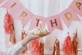 Happy Birthday. Hand holding delicious birthday donut with candle in room with pink garland Royalty Free Stock Photo