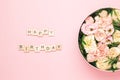 Happy birthday lettering on the wooden squares with letters on the pink background and big round box with red flowers