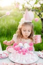Happy birthday little girl making wish blowing candles on cake with pink decor in beautiful garden Royalty Free Stock Photo