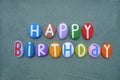 Happy Birthday message composed with hand painted multi colored stone letters over green sand