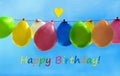 Happy birthday, multi colored balloons hanging in front of blue Royalty Free Stock Photo