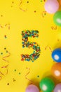 Happy Birthday number 5 made of candies with colorful balloons on yellow background