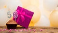 Happy birthday with a pink gift box for a 56 year old woman. Beautiful birthday card with cupcake and burning candle number fifty Royalty Free Stock Photo