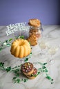 Happy birthday ring cake, cookies, biscuits, muffins and champagne  with clover decoration on marble table and lilac background Royalty Free Stock Photo