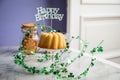 Happy birthday ring cake, cookies, biscuits, muffins and champagne  with clover decoration on marble table and lilac background Royalty Free Stock Photo