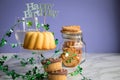 Happy birthday ring cake, cookies, biscuits, muffins and champagne  with clover decoration on marble table and lilac background Royalty Free Stock Photo