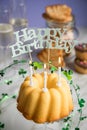 Happy birthday ring cake, cookies, biscuits, muffins and champagne  with clover decoration on marble table and lilac background Royalty Free Stock Photo