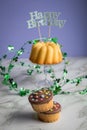 Happy birthday ring cake and muffins with clover decoration on marble table and lilac background Royalty Free Stock Photo