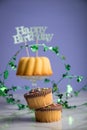 Happy birthday ring cake and muffins with clover decoration on marble table and lilac background Royalty Free Stock Photo