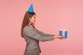 Happy birthday, take present! Side view of happy woman in business suit and with party cone on her head