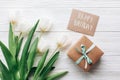 happy birthday text sign on stylish craft present box and greeting card and tulips on white wooden rustic background. flat lay wi Royalty Free Stock Photo