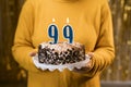 Happy birthday. Woman holding fresh delicious birthday cake with burning candle number 99, close up. Celebration of