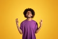 Happy black adult curly man in purple t-shirt and glasses makes cross fingers gesture