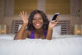 Happy black African American woman sitting on bed using internet mobile phone smiling cheerful and relaxed networking online Royalty Free Stock Photo