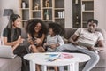 Happy black african family enjoy holiday together at sofa living room two daughter playing game mother online working with laptop Royalty Free Stock Photo