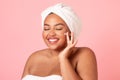 Happy black body positive woman applying beauty product on her face and smiling, lady wrapped in towel using face cream Royalty Free Stock Photo