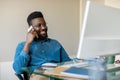 Happy black businessman having phone conversation with client, sitting in front of computer and talking on cellphone Royalty Free Stock Photo