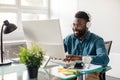 Happy black businessman in headset working on computer, making conference video call, sitting in office Royalty Free Stock Photo