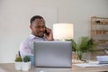 Happy black businessman talking on cellphone having phone conversation sitting at workplace working on laptop computer Royalty Free Stock Photo