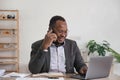Happy black businessman talking on cellphone having phone conversation sitting at workplace working on laptop computer Royalty Free Stock Photo