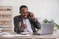 Happy black businessman talking on cellphone having phone conversation sitting at workplace working on laptop computer Royalty Free Stock Photo