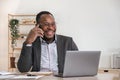 Happy black businessman talking on cellphone having phone conversation sitting at workplace working on laptop computer Royalty Free Stock Photo