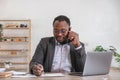 Happy black businessman talking on cellphone having phone conversation sitting at workplace working on laptop computer Royalty Free Stock Photo