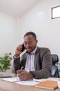 Happy black businessman talking on cellphone having phone conversation sitting at workplace working on laptop computer Royalty Free Stock Photo