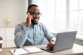 Happy black businessman talking on cellphone sitting at workplace indoors Royalty Free Stock Photo