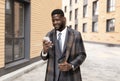 Happy black businessman texting on cellphone and drinking takeaway coffee, walking outside office building Royalty Free Stock Photo