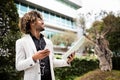 Happy black businessman using cellphone and listening music in earphones, standing outdoors in park near office Royalty Free Stock Photo