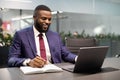 Happy black businessman using laptop and taking notes Royalty Free Stock Photo