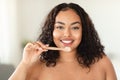 Happy black chubby woman standing in bathroom, brushing her teeth in the morning, looking at camera Royalty Free Stock Photo