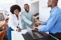 Happy black couple buying new car, shaking hands with seller, signing auto purchase agreement at dealership