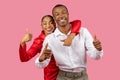 Happy black couple giving thumbs up, woman in red, man in white, pink background Royalty Free Stock Photo