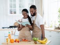 Happy black couple reading recipe in cookbook while cooking lunch in kitchen Royalty Free Stock Photo