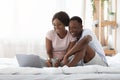 Happy black couple sitting on bed, watching movie on laptop