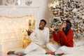 Portrait of happy black couple throwing gifts in the air while sitting near Christmas tree Royalty Free Stock Photo