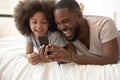 Happy black dad use phone laugh on bed with daughter Royalty Free Stock Photo