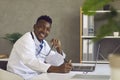 Young black doctor sitting at office desk with laptop, looking at camera and smiling Royalty Free Stock Photo