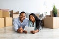 Happy black family lying on floor in new apartment with digital tablet among cardboard boxes with belongings Royalty Free Stock Photo