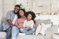 Happy black family of three hugging on couch and smiling