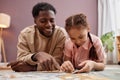 Happy Black father solving jigsaw puzzle with little girl