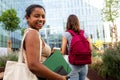 Happy Black female college student standing outside university building holding notebooks in campus looking at camera. Royalty Free Stock Photo